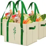 Tri veľké kapacity netkaných piknikových nákupných tašiek naplnené rôznymi potravinami, vrátane čerstvej zeleniny a chleba.