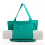Women's Yoga Fitness Tote in teal with exterior pocket holds a rolled-up white yoga mat, zobrazené na bielom pozadí. K dispozícii sú možnosti OEM a ODM.