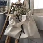 Borża tax-xiri tal-kanvas li tiġbed bil-wildflowers ġewwa, Imdendel fuq sellum tal-injam minn tieqa - ideali għall-wiri ta 'disinji OEM ODM fi stil ta' kuljum.