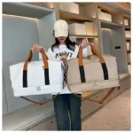 Mae menyw mewn cap yn dal ffasiwn gwyn Bag Teithio Rhydychen Gwrth -ddŵr yn ei Llaw Chwith a Bag OEM llwydfelyn yn ei llaw dde.