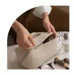 Особа отвара преносну водоотпорну врећу за шминкање кумерне плоче на столу са четкицама са шминкањем и боцом за распршивање.