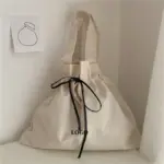 Minimalist Canvas Drawstring Tote for Women in beige with black ribbon and "LOGO" texte, Dissenyat per a OEM/ODM, es mostra en una superfície blanca a prop d'una il·lustració de préssec.