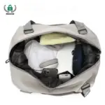 Nangungunang view ng isang bukas na magaan na malaking kapasidad na tote ng paglalakbay na may hawak na tuwalya, mga headphone, Telepono, Charger, at nakatiklop na damit - perpekto para sa mga pagpipilian sa pagpapasadya ng ODM OEM.