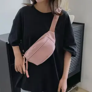 Person wearing a loose black t-shirt and an Adjustable Sporty Crossbody Bag in light pink, standing indoors, highlighting trendy OEM ODM fashion.