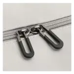 Close-up ng dalawang itim na siper ay kumukuha sa isang light grey na background ng tela, Ang pag-highlight ng kalidad ng OEM ODM ng magaan na malaking kapasidad na tote ng paglalakbay.